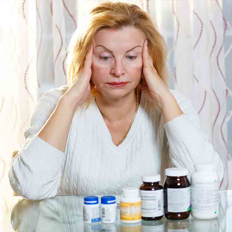 An older woman who looks stressed and has six bottles of prescription pills in front of her.