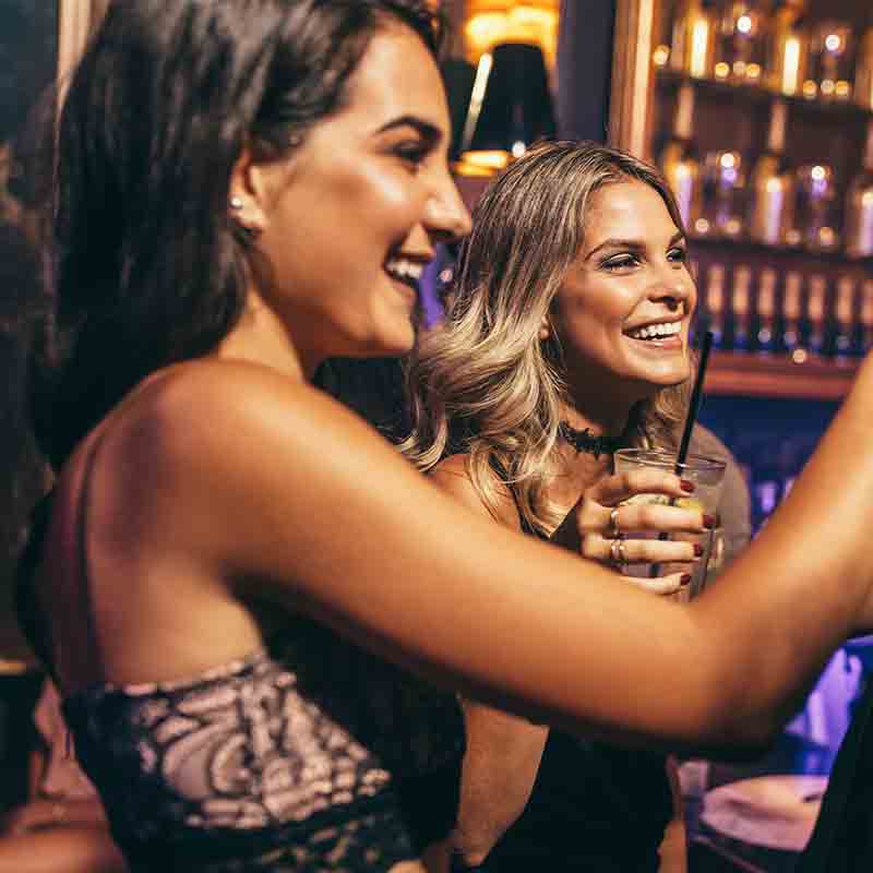 A picture of two beautiful women drinking alcohol at a club.